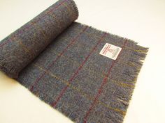 "HARRIS TWEED FRINGED SCARF Handmade in Scotland by The Little Stitch Company  25cm wide 200cm long Keep warm this winter with a cosy Harris Tweed scarf.   At 2 metres long, the scarf is longer than most Harris Tweed scarves.  This gives you greater flexibility in how you wear it.  Keep it casual with one end thrown over your shoulder.  Wrap it round your neck to keep warm and cosy.  Or double it over and pull the ends through the loop for a more modern look.   The scarf is made from handwoven Harris Tweed - a pure, new wool fabric - in a muted blue with a fine overcheck of red and yellow..  It's fringed on all sides with deeper fringing at the ends. It carries the Harris Tweed Authority's orb label which is your guarantee of authenticity - please scroll down for more information about Har Tweed Scarf Pattern, Tweed Scarf, Woven Scarves, Fringe Scarf, Harris Tweed, Wool Fabric, Keep Warm, Look Plus, Scarf Wrap