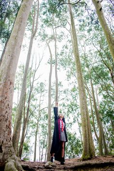 a woman standing in the middle of a forest holding her arms up to the sky