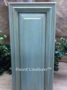 a green cabinet sitting on top of a floor next to a plant filled with flowers