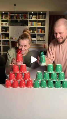 a man and woman sitting at a table with stacks of cups in front of them