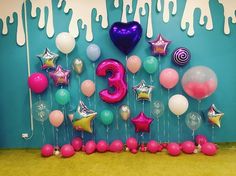 the number three surrounded by balloons and streamers in front of a blue wall with white drips