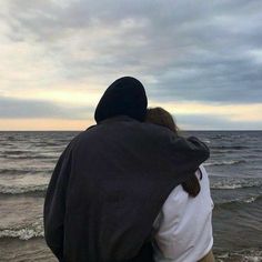 two people standing on the beach looking out at the ocean