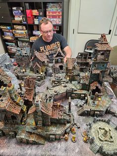 a man sitting at a table in front of a bunch of small model houses and buildings