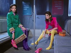 two women sitting on a subway car, one in green and the other in pink