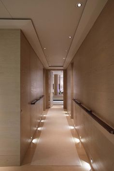 an empty hallway with lights on the walls and wood paneling along one wall, leading to another room