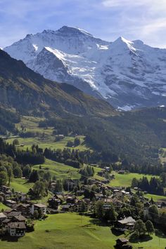 the mountains are covered in snow and green grass, with houses nestled on each side