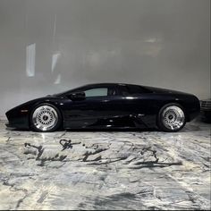 a black sports car sitting on top of a marble floor in front of a wall