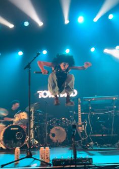 a man is jumping in the air on top of a stage with drums and microphones