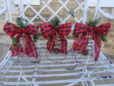 two red and black plaid bows are attached to bells on a white rocking chair with greenery