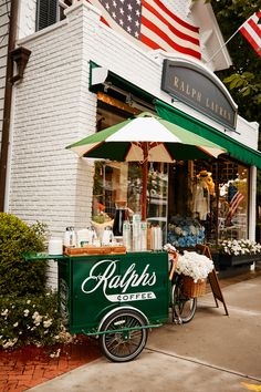 an outdoor coffee cart on the side of a street with flowers in front of it