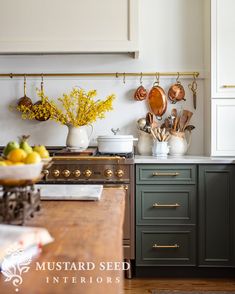 a kitchen with green cabinets and gold handles on the counter top, along with hanging utensils