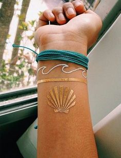 a woman's arm with a gold shell on it and green string bracelets