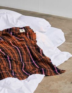 an orange and black plaid blanket laying on top of a white sheet covered in paper