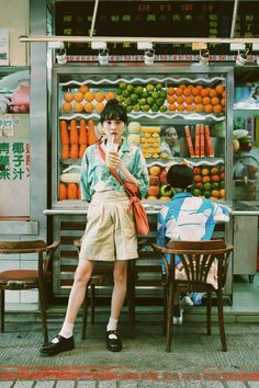 a person sitting at a table with an umbrella in front of a fruit stand on the street