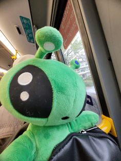 a green stuffed animal sitting on top of a black bag