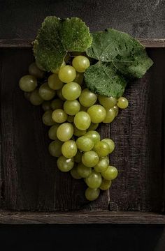 a bunch of green grapes sitting on top of a wooden table next to a leaf