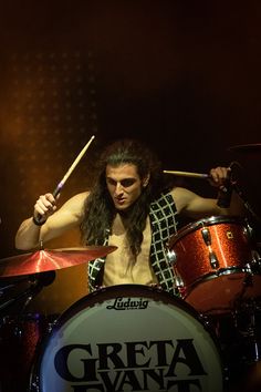 a man with long hair playing drums on stage