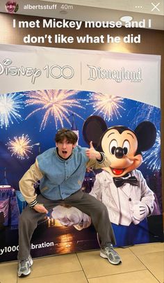 a man standing in front of a mickey mouse sign with fireworks coming out of it