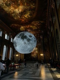 people are walking around in an ornate building with a large moon hanging from the ceiling