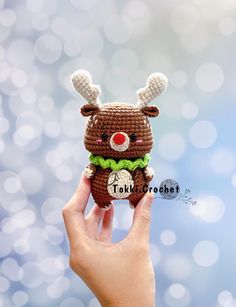 a hand holding up a small crocheted toy with a deer on it's face