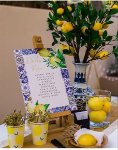 a table topped with lemons next to a vase filled with yellow flowers and greenery