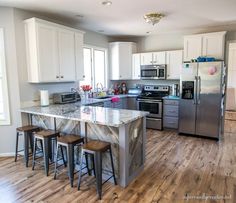 a kitchen with white cabinets and marble counter tops, stainless steel appliances and stools