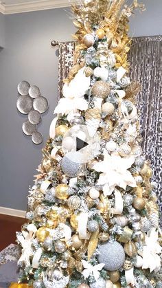 a white christmas tree with gold and silver ornaments on it's top, in front of a window