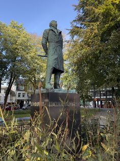 a statue of a man with a hat and coat in the middle of a park