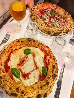 two pizzas sitting on top of a table next to silverware and glasses filled with drinks