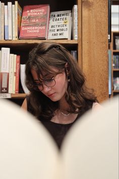 a woman reading a book in front of a bookshelf