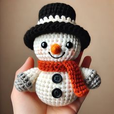 a small crocheted snowman wearing a black hat and orange scarf with buttons