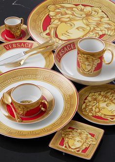 a table topped with plates and cups filled with gold colored dishes covered in versa design