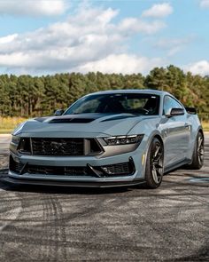 the front end of a silver mustang on a race track with trees in the background