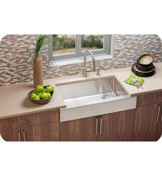 a kitchen sink sitting under a window next to a bowl of green apples and a vase