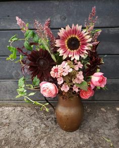 a vase filled with lots of flowers on top of a cement floor next to a wooden wall