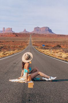 a woman sitting on the side of an empty road with mountains in the back ground