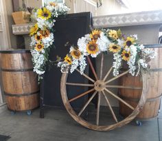 an old wagon with sunflowers and daisies on the wheels is sitting in front of some barrels