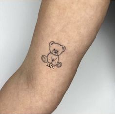 a small tattoo on the arm of a person with a teddy bear sitting next to it