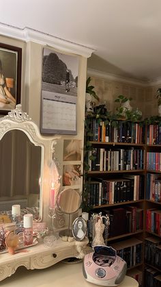 a desk with a mirror, lamp and other items on it in front of a bookshelf