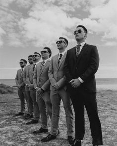 a group of men standing next to each other wearing suits and sunglasses on top of a grass covered field