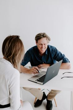 a man and woman sitting at a table with laptops in front of each other