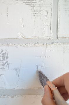 a person holding a paintbrush in front of a white wall with peeling paint on it