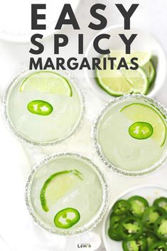 three margaritas with lime slices and sliced jalapenos in them on a white surface