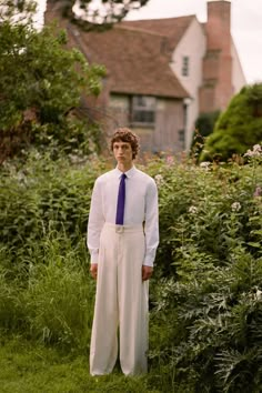 a man standing in the grass wearing a white shirt and tie with wide legged pants