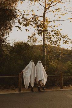 two people in white ghost costumes walking down the street