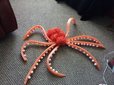 an orange and white octopus made out of plastic beads on the floor next to a couch