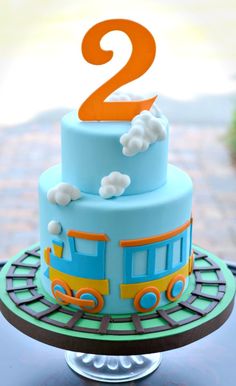 a blue and yellow train cake with clouds on it's top is sitting on a table