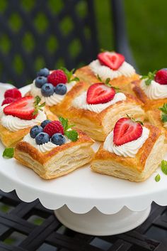 a white plate topped with pastry covered in cream and berries on top of a table