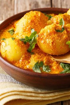 a wooden bowl filled with potatoes covered in sauce and garnished with parsley