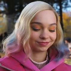 a woman with blonde hair wearing a pink jacket and blue eyeshadow is looking at her cell phone